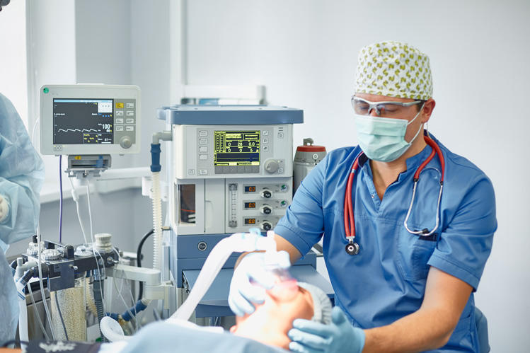 Anesthesiologist monitoring patient at surgical anesthesia cart